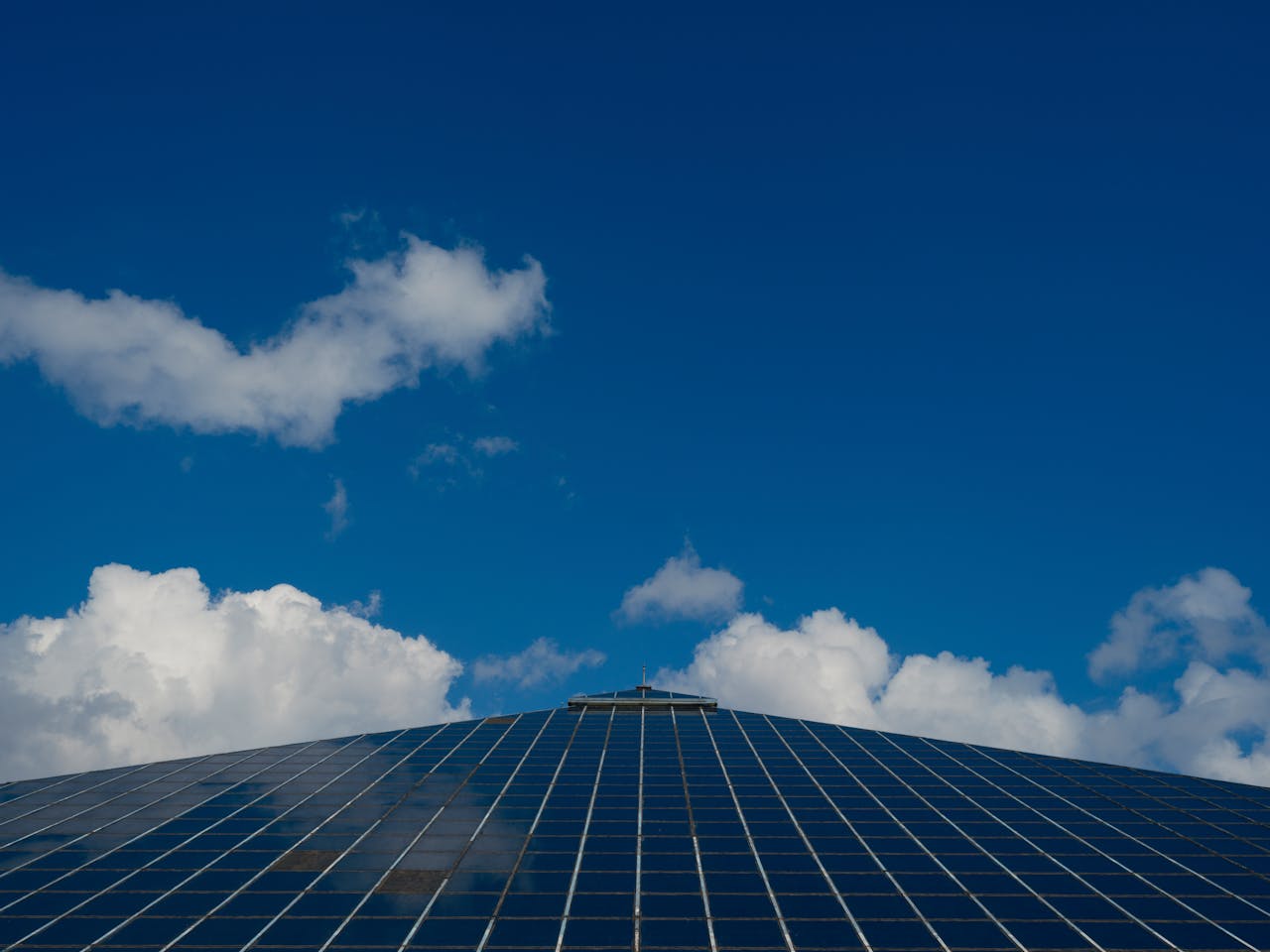 Solar panels reflecting a clear blue sky with scattered clouds, symbolizing renewable energy.